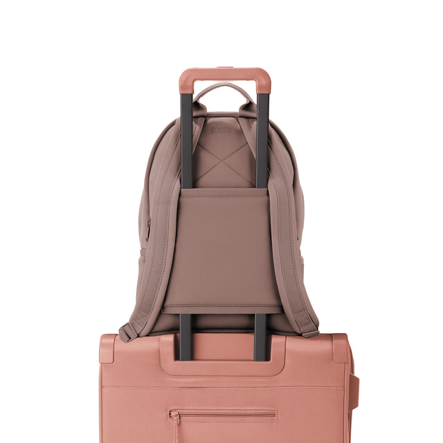 Dagne Dover medium Dakota Neoprene Backpack in pink strapped to luggage with the neoprene luggage-handle sleeve.