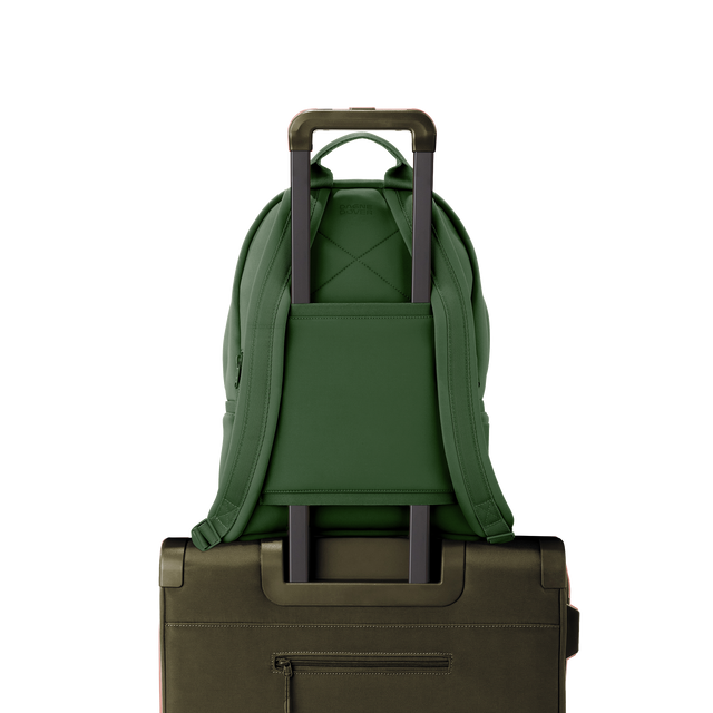 Dagne Dover medium Dakota Neoprene Backpack in a rich, classic forest green strapped to luggage with the neoprene luggage-handle sleeve.
