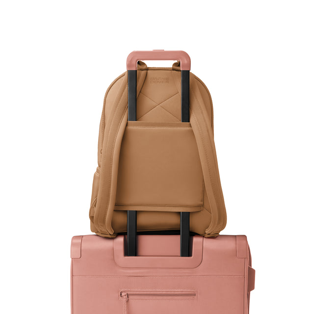 Dagne Dover large Dakota Neoprene Backpack in camel brown strapped to luggage with the neoprene luggage-handle sleeve.