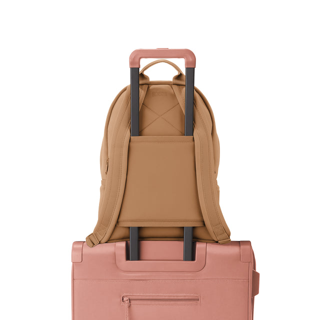 Dagne Dover medium Dakota Neoprene Backpack in camel brown strapped to luggage with the neoprene luggage-handle sleeve.