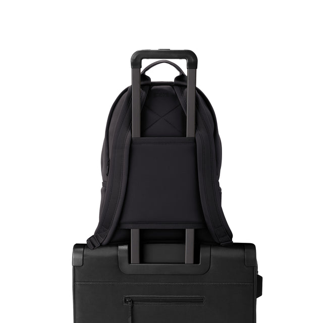 Dagne Dover medium Dakota Neoprene Backpack in black strapped to luggage with the neoprene luggage-handle sleeve.