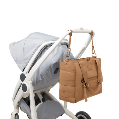 Dagne Dover large Wade Diaper Tote in camel brown strapped to the handle of a stroller.