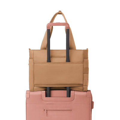 Dagne Dover large Wade Diaper Tote in camel brown with the neoprene luggage sleeve attached to a suitcase handle.