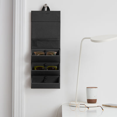 Dagne Dover Remi foldable glasses holder in black hung up and holding glasses by a desk.